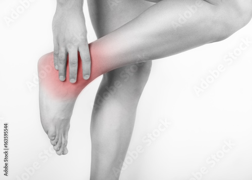 Close up view of a young man holding his ankle in pain, isolated on white background. Lower leg pain. Young man touching his ankle for the pain. Red inflammation effect.