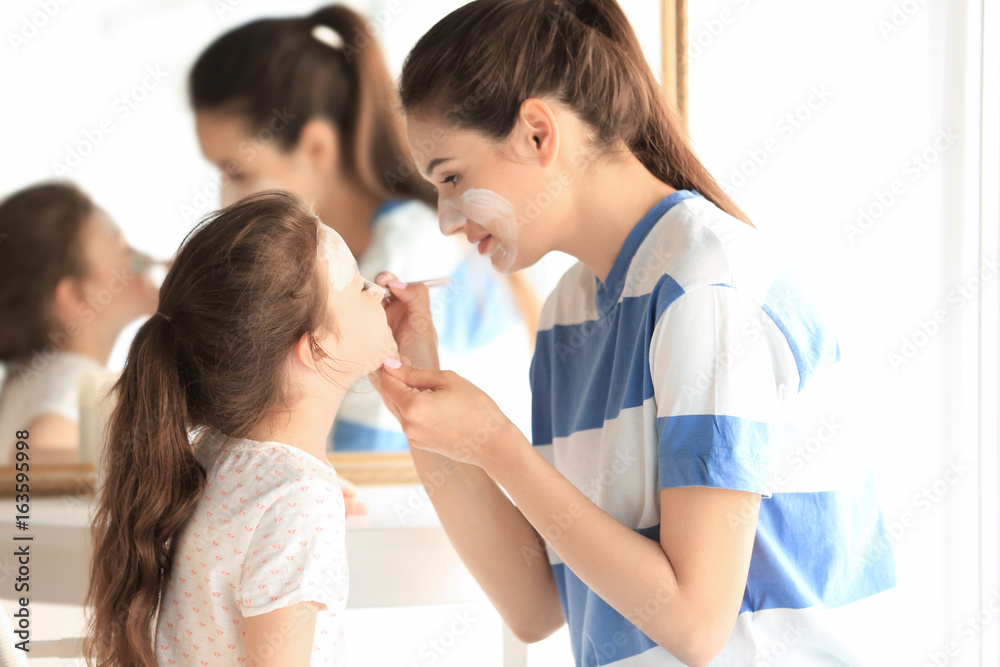 Young woman and her little daughter applying facial mask at home Young woman and her little daughter applying facial mask at home