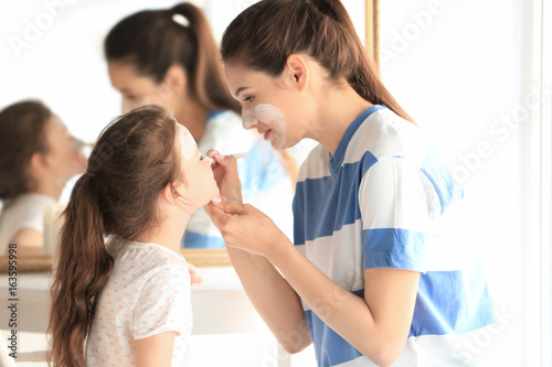 Young woman and her little daughter applying facial mask at home
