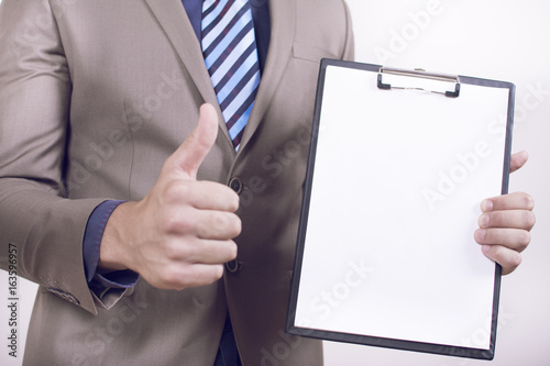 Close up view of a young businessman holding his clipboard toward the camera white background. Copy space on the paper. Close-up of a man giving thumb up.