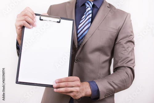 Close up view of a young businessman holding his clipboard toward the camera white background. Copy space on the paper. Close-up of a man holding white paper.