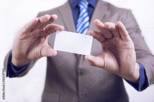 Close up view of a young businessman holding his business camera toward the camera white background. Copy space on the card. Close-up of a man giving a business card.