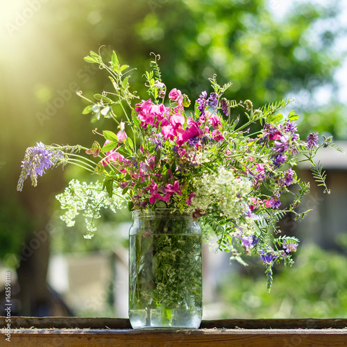 A bouquet of fresh bright and fragrant flowers in a glass transparent jar on a wooden window sill against the backdrop of a garden