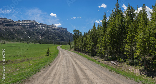 Dirt road leads through a vast mountain meadow in a Rocky Mountains wilderness in the western United States.