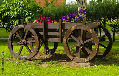 Old wooden wagon with flowers. Rustic decoration. Decorative trolley in retro style. The concept of landscape design in the park.