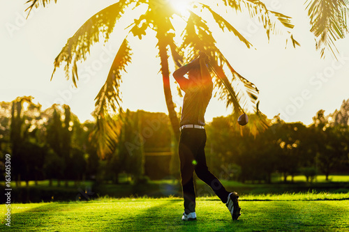 asian man playing golf on a golf course against sunset