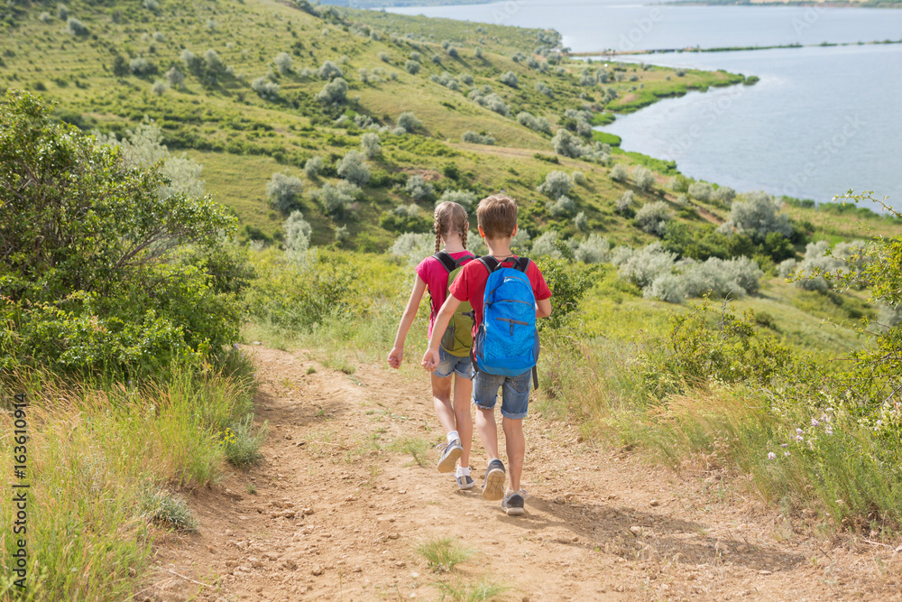 Teen boy and girl with backpacks on the back go on a hike, travel, beautiful landscape
