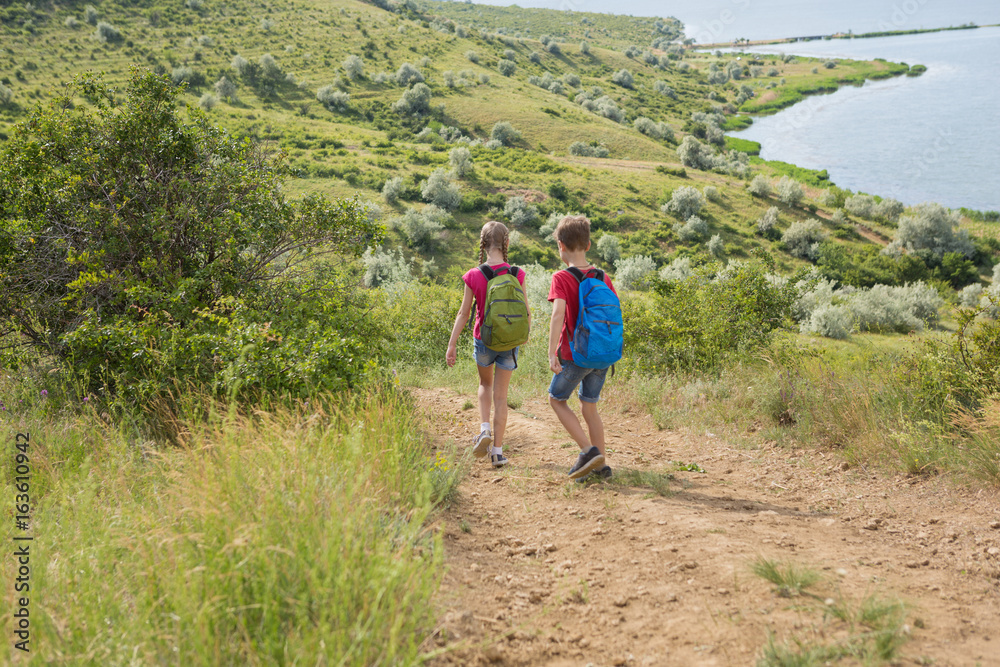 Teen boy and girl with backpacks on the back go on a hike, travel, beautiful landscape