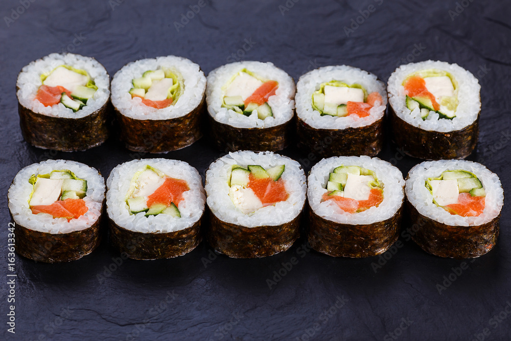 Appetizing fresh maki sushi roll with salmon and tofu cheese served on black slate, close up. Japanese healthy seafood.