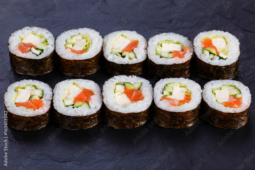Appetizing fresh maki sushi roll with salmon and tofu cheese served on black slate, close up. Japanese healthy seafood. Appetizing fresh maki sushi roll with salmon and tofu cheese served on black slate, close up. Japanese healthy seafood.