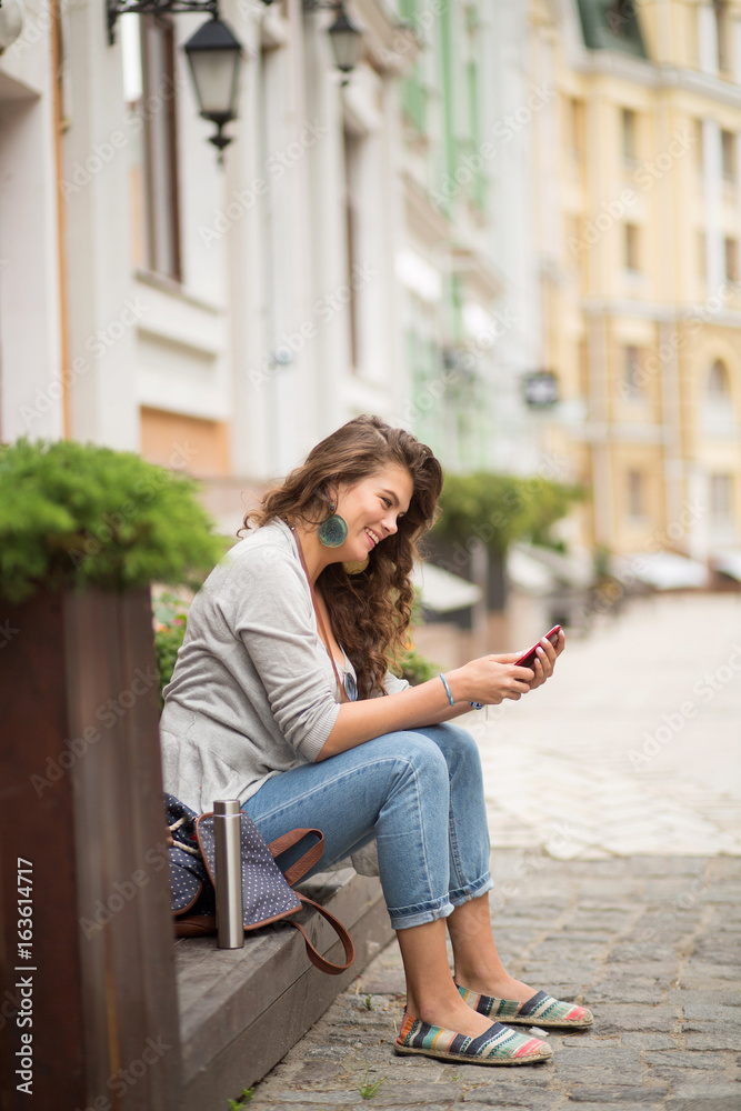 Tourist young woman sitting on stairs in the street. Female having rest after long walk, watching in phone.
