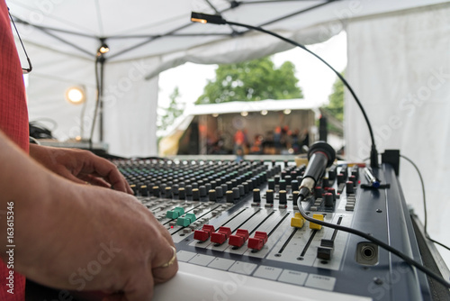 Sound mixer at an open air music festival, view over the mixing panel with sliders and microphone, stage blurred in the background