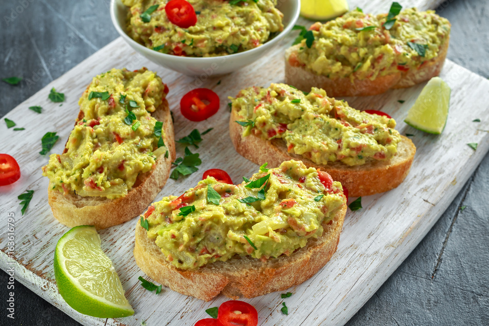 Homemade Guacamole toast with chili pepper, parsley on white wooden board Homemade Guacamole toast with chili pepper, parsley on white wooden board