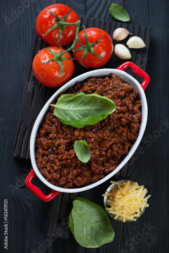 Top view of freshly made bolognese sauce with some of its cooking components on a black wooden background