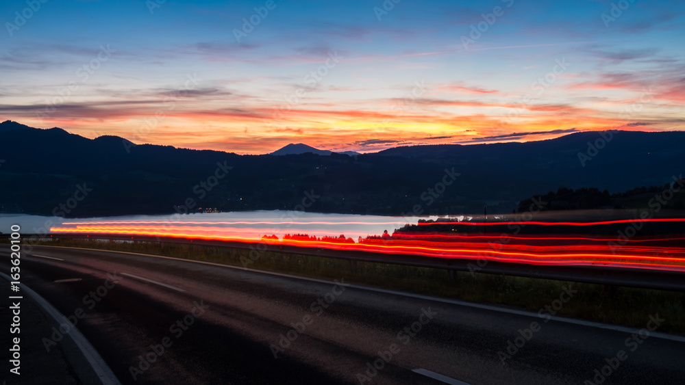 Austrian countryside road car is passing during the sunset only light rays are visible lacke is on the background