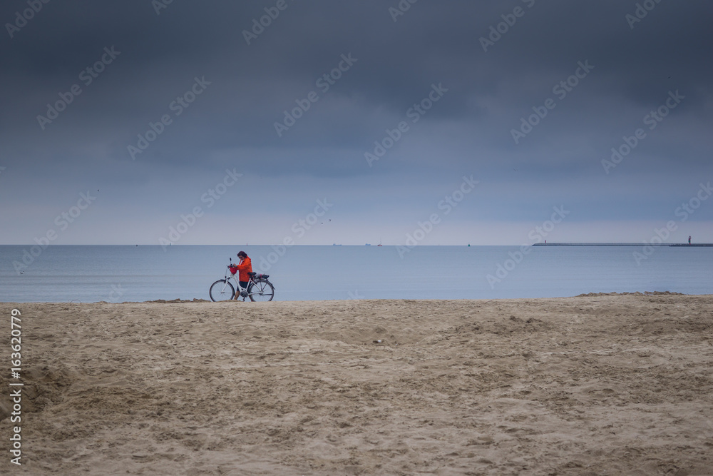 a woman ride a bike by the sea on a cloudy day