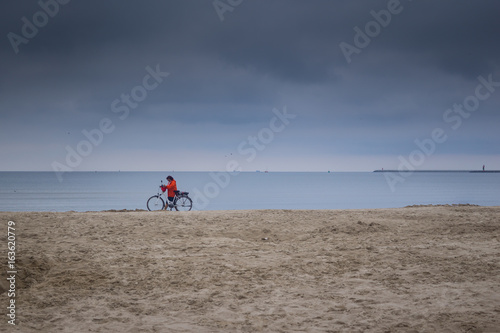 a woman ride a bike by the sea on a cloudy day