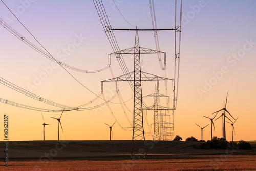Green energy concept - high voltage power lines with a windmill farm background