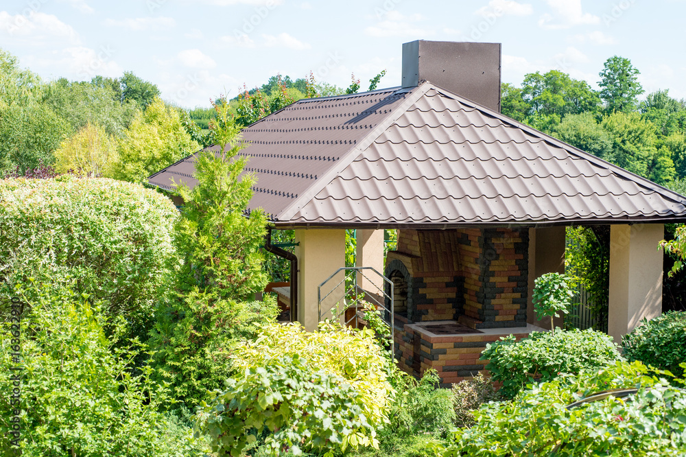 Gazebo with place for barbecue in a juicy green summer garden