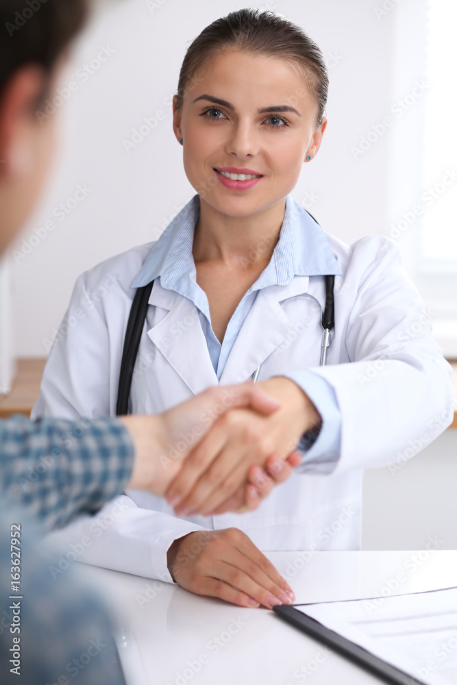 Doctor woman smiling while shaking hands with her male patient. Medicine and trust concept Doctor woman smiling while shaking hands with her male patient. Medicine and trust concept
