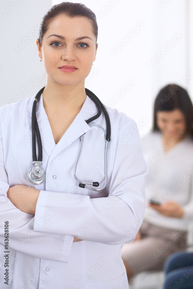 Brunette female doctor on the background of colleagues talking to each other in hospital. Physician is ready to help patients. Medicine and health care concept Brunette female doctor on the background of colleagues talking to each other in hospital. Physician is ready to help patients. Medicine and health care concept
