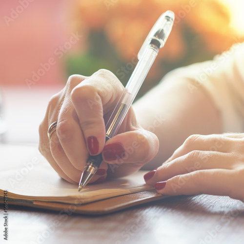 woman's hand with red nails writing some message note or letter to notebook by pen