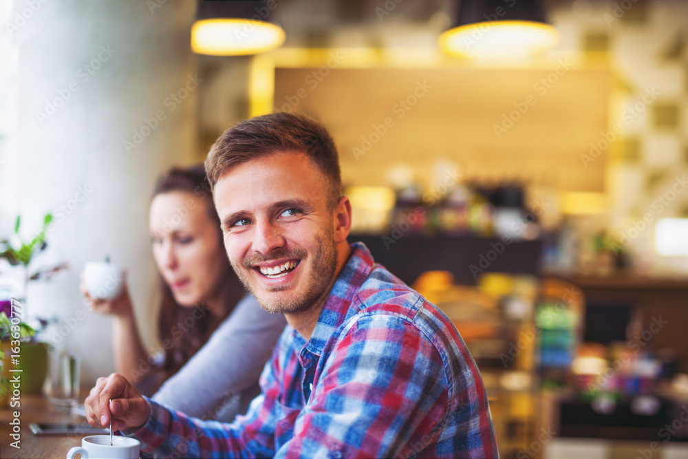 Young smiling couple drinking coffee in a cafeteria. Focus on man