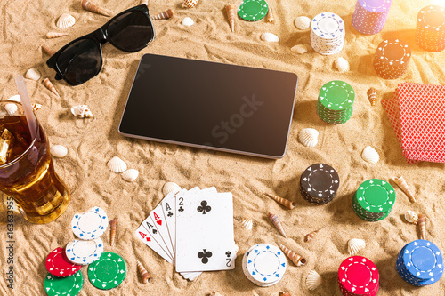 Online poker game on the beach with digital tablet and stacks of chips. Top view