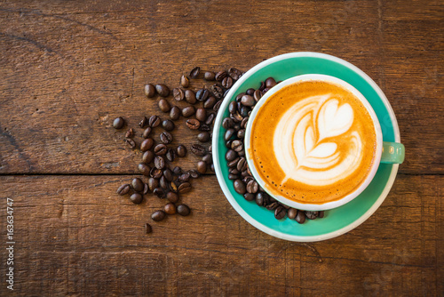 Top view of Cappuccino hot coffee in a green cup with latte art and roasted coffee beans on wooden table background.