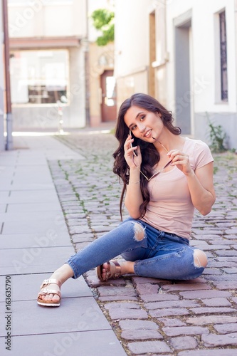 Young beautiful woman brunette walks at the city in Europe. Summer. Happy girl. Street fashion. Young beautiful woman speaks by phone. The girl takes pictures of herself.