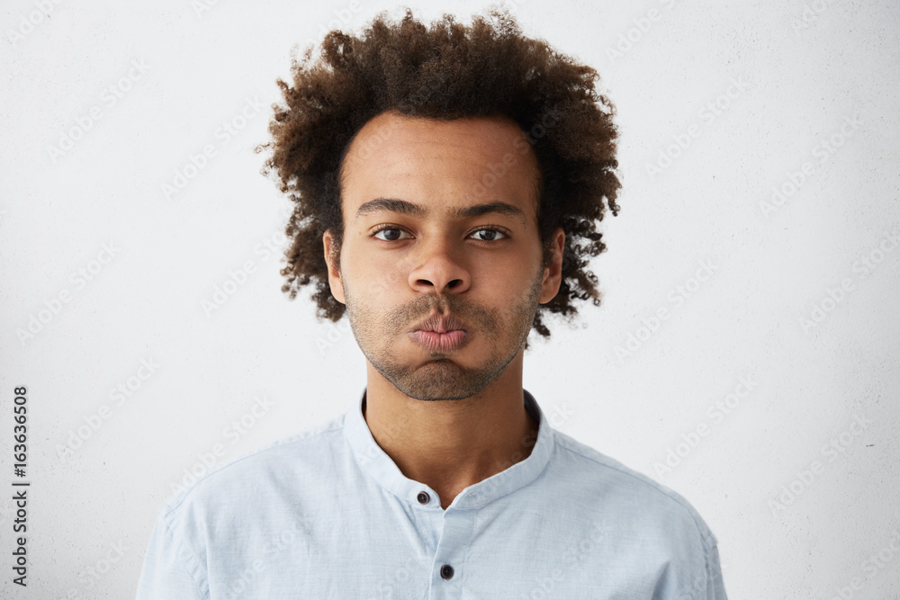 Young handsome man with curly dark hair blowing his cheeks while being offended at somebody showing his negative emotions and resentment. Resentful mixed race man in formal clothes isolated over white Young handsome man with curly dark hair blowing his cheeks while being offended at somebody showing his negative emotions and resentment. Resentful mixed race man in formal clothes isolated over white