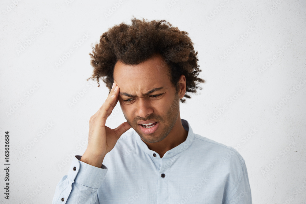 Φωτογραφία Stressful Afro American male with bushy hair frowning his face holding hand on temple having headache having frustrated expression