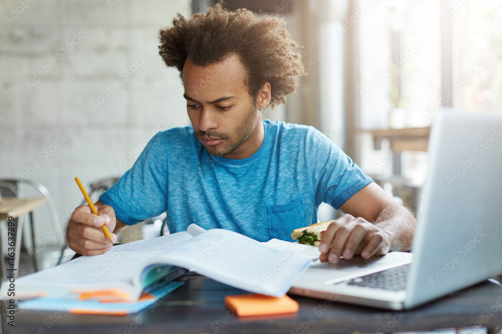 Φωτογραφία Candid shot of concentrated Afro American hipster male in blue T-shirt preparing