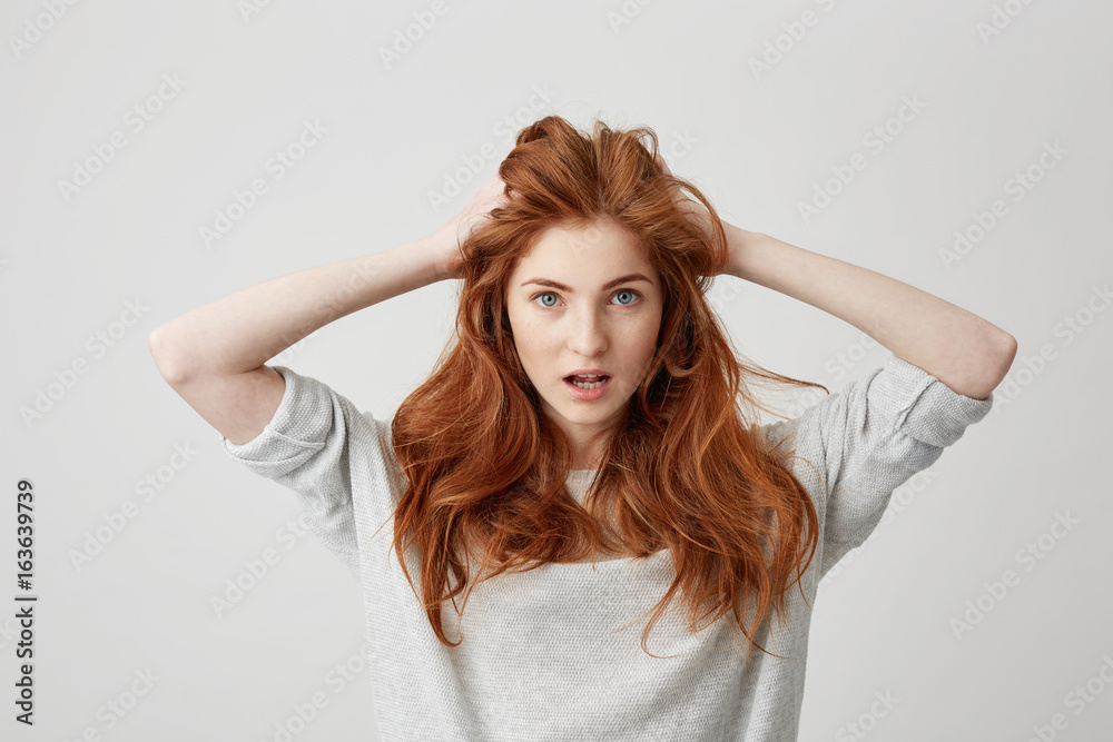 Naklejka premium Portrait of surprised redhead beautiful girl looking at camera with opened mouth touching head over white background.