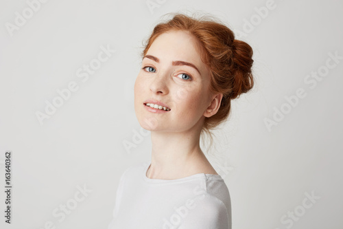 Portrait of young beautiful redhead girl with freckles looking at camera smiling over white background.