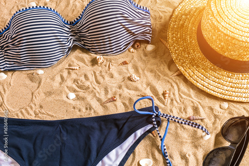 Summer bikini and accessories stylish beach set, Beach bikini summer outfit and sea sand as background, Top View, Concept photo