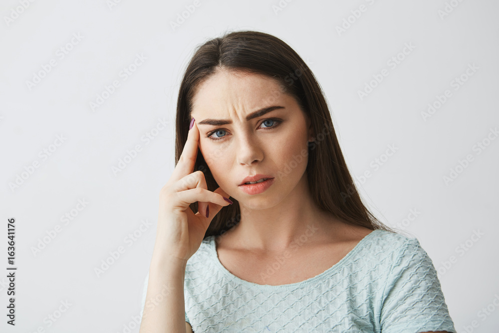 Portrait of young beautiful girl looking at camera frowning thinking with finger on temple over white background. Portrait of young beautiful girl looking at camera frowning thinking with finger on temple over white background.