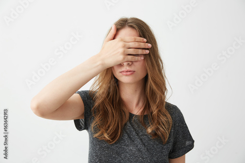 Young pretty girl covering closing eyes behind hand over white background.