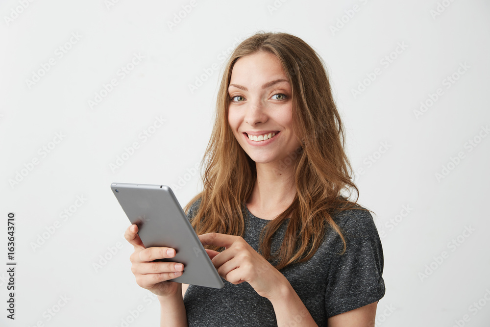 Young pretty girl smiling looking at camera surfing web browsing internet on tablet over white background. Young pretty girl smiling looking at camera surfing web browsing internet on tablet over white background.