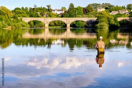 Man fly-fishing on the River Tweed with the iconic Kelso Bridge at the background. Kelso, Scottish Borders, Scotland, UK