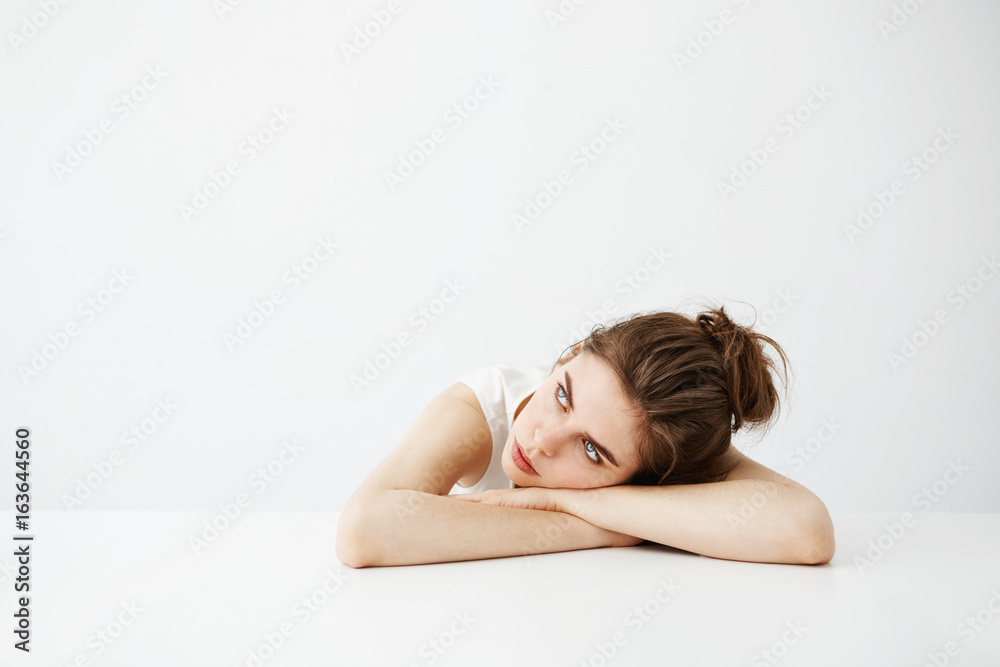 Bored tired young pretty girl with bun thinking dreaming lying on table over white background. Bored tired young pretty girl with bun thinking dreaming lying on table over white background.