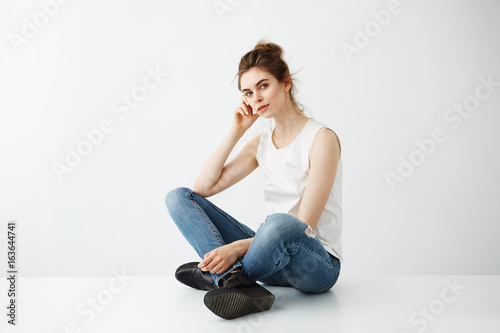 Young beautiful brunette girl with bun smiling looking at camera sitting over white background.