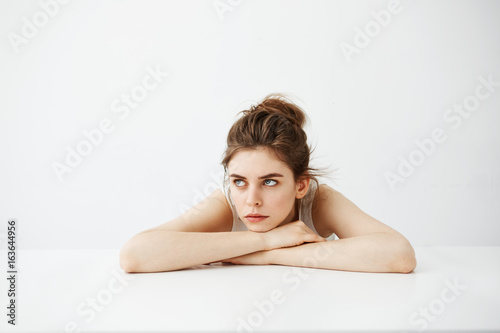 Bored tired young pretty girl with bun thinking dreaming lying on table over white background.