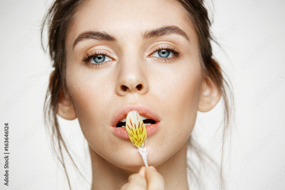 Close up of beautiful young girl with perfect clean skin and alstroemeria petals looking at camera over white background. Facial treatment. Beauty and spa. Close up of beautiful young girl with perfect clean skin and alstroemeria petals looking at camera over white background. Facial treatment. Beauty and spa.