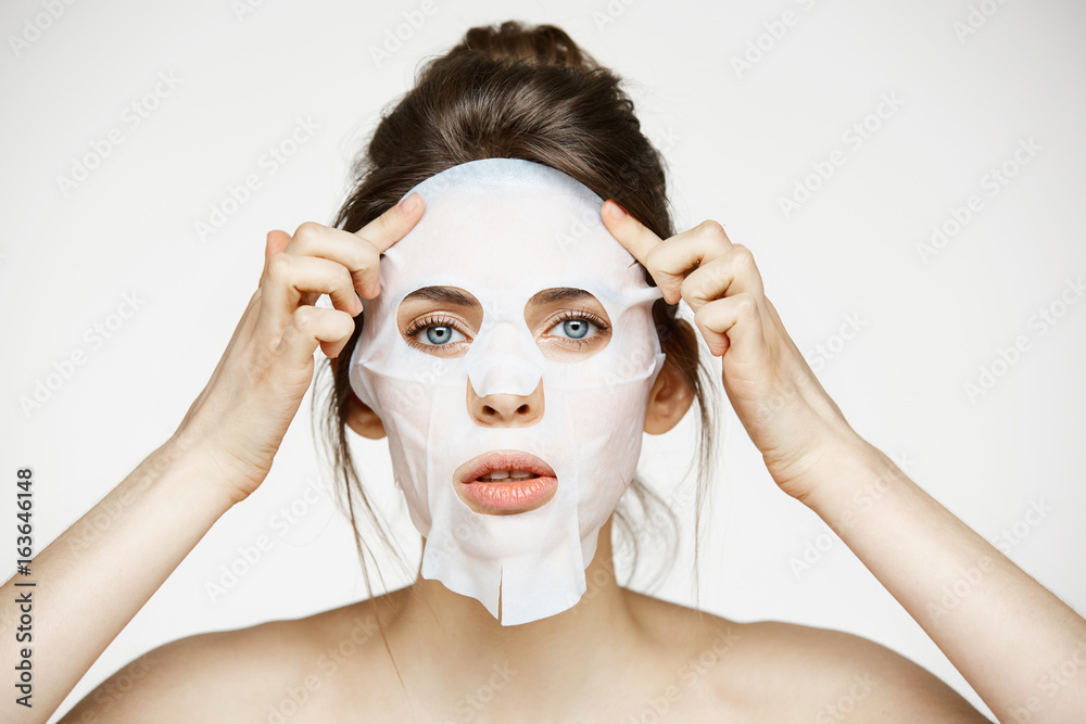 Young girl with facial mask looking at camera over white background. Cosmetic procedure. Beauty spa and cosmetology. Young girl with facial mask looking at camera over white background. Cosmetic procedure. Beauty spa and cosmetology.