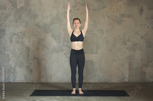 Young woman practicing yoga Mountain pose, Samasthiti against texturized wall / urban background