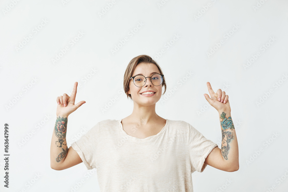 Young beautiful girl in glasses smiling looking at camera pointing fingers up over white background. Young beautiful girl in glasses smiling looking at camera pointing fingers up over white background.