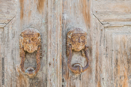 Old, rusty handles with Egyptian motifs on a weathered wooden door. Lindos, Rhodes, Greece