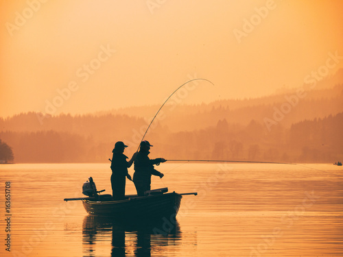 Fotografia Silhouette of man fishing on lake from boat at sunset