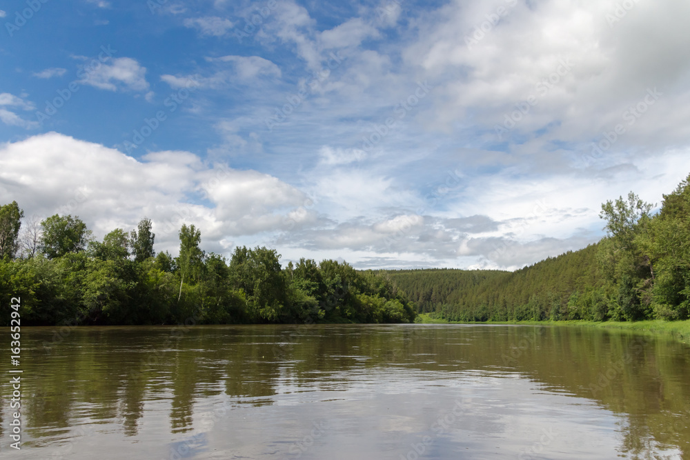 The high water on the river Ufa in the summer. Green trees and blue sky with clouds.